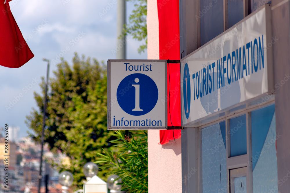 Wall mural tourist information sign with information symbol hanged in front of an information desk. trees and p
