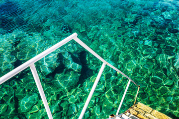 Staircase in clear turquoise water with sun flare. Close-up. Relax and calm. Space for text.