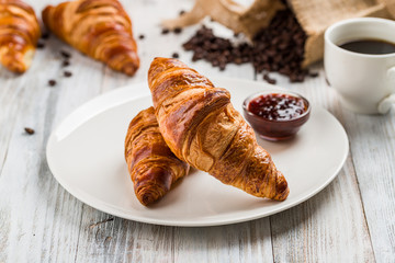 Classic croissants on a white plate with jam on a light wooden background