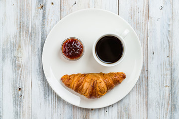 Coffee with croissant and jam on a light wooden background top view