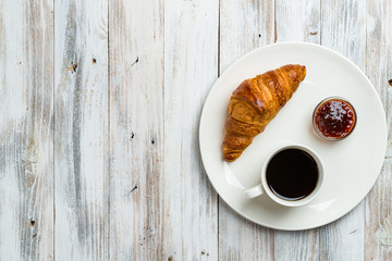 Coffee with croissant and jam on a light wooden background with copy space