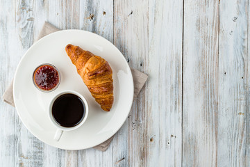 Coffee with croissant and jam on a light wooden background with copy space