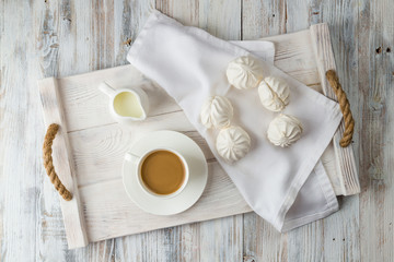 Coffee and white marshmallows on a light wooden tray top view