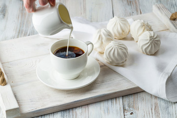 milk is poured into the coffee on a light wooden tray with marshmallows