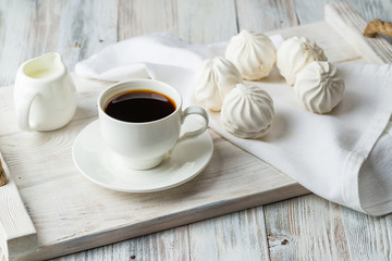 Coffee and white marshmallows on a light wooden tray