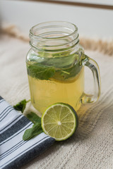 homemade lemonade made of water, lemonade, mint and lime on a light background. Mojito in a cocktail mug with a lid and a straw