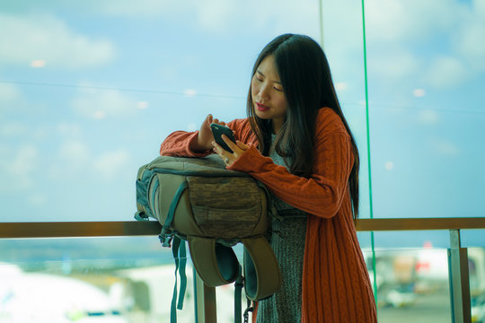 young beautiful and happy Asian Chinese woman checking mobile phone at airport departure lounge carrying backpack waiting for boarding smiling cheerful ready for holiday travel