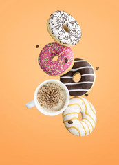 Creative poster with donuts. Doughnuts in motion falling on orange background. Sweet donuts with white cup coffee flying in motion or falling.