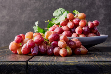 Fresh grapes. Bunches of different varieties in a plate on an old wooden table and dark background. soft focus