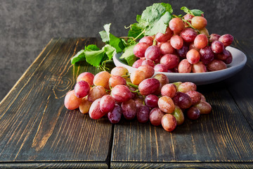 Fresh grapes. Bunches of different varieties in a plate on an old wooden table and dark background. soft focus