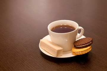 cup of black tea on a saucer with bagels, waffles and cookies