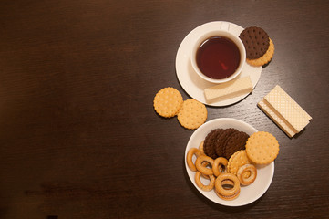 cup of black tea on a saucer with bagels, waffles and cookies