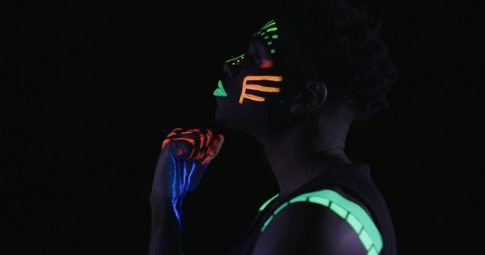 Studio, slow motion, close-up of a neon-painted dancer posing with his hands