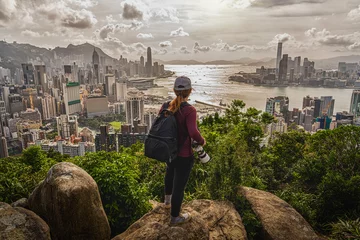 Foto op Plexiglas Back side of asia woman photographer standing and shooting after climbing the peak of hong kong mountain and looking hong kong and kowlloon cityscape at sunset time,adventure and travel concept © THANANIT