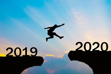 Happy New Year 2020 Men jump over silhouette mountains sun