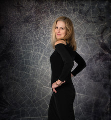 Sexy confident middle aged woman in black dress posing in front of halloween style wall