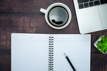 Workspace with an empty notebook, coffee, and a computer on a wooden desk
