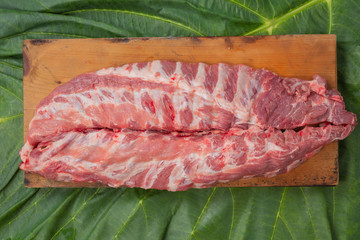 Pork ribs placed on a wooden cutting board with a green leaf background.