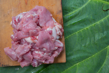 Pork that is placed on a wooden cutting board with a green leaf background.