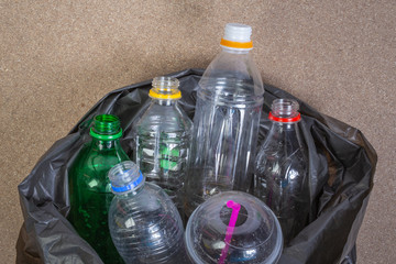 Used water bottles that are in black garbage bags on a brown plywood background.