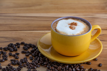 Hot cappuccino coffee in a yellow glass placed on the plank floor.
