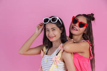 Two Asian girls who are friends are happy and have a pink background.