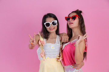 Two Asian girls who are friends are happy and have a pink background.