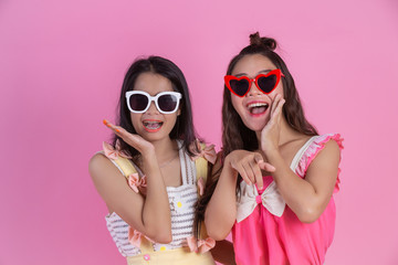 Two Asian girls who are friends are happy and have a pink background.