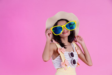 A beautiful Asian woman wearing a hat and large glasses with a pink background.