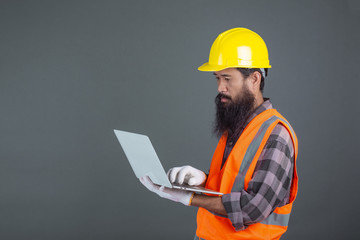 An engineering man wearing a yellow helmet holding a notebook on a gray background.