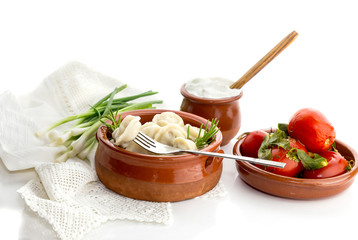Boiled dumplings in a bowl, sour cream and pickled tomatoes close-up (russian and ukrainian cuisine)