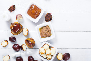 medicine cream, ground conkers tincture with alcohol and sliced seeds from horse chestnuts, on white wooden table