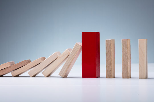 Red Wooden Block Amidst Falling And Upright Domino Pieces