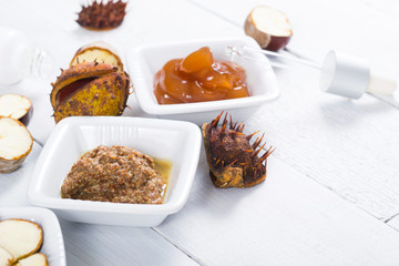 medicine cream, ground conkers tincture with alcohol and sliced seeds from horse chestnuts, on white wooden table