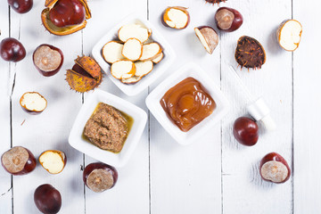 medicine cream, ground conkers tincture with alcohol and sliced seeds from horse chestnuts, on white wooden table