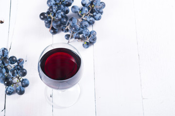 glass of red wine and blue grapes on white wooden table background