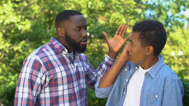 Angry male hitting son upside head shouting outdoors, parenting difficulties