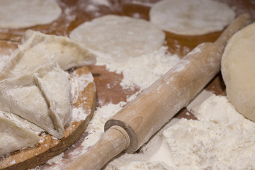 dough, rolling pin and pies of dough with meat on a table with flour