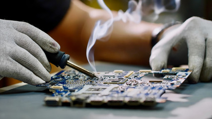 Technician engineer in workshop. Repairman in gloves is soldering circuit board of electronic...