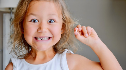 Portrait of cute little cheerful child girl is showing her lost milk tooth and smiling to camera of...