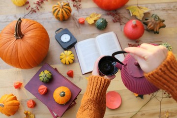 Autumn tea.Autumn flat lay. Thanksgiving Day. Female hands in a brown sweater pour tea from a red...