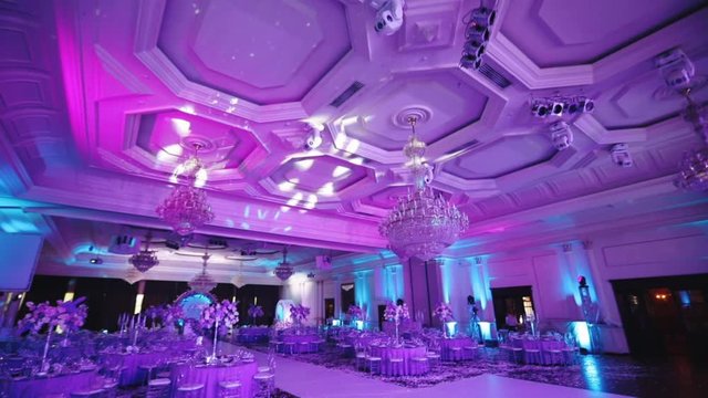 wonderful wedding hall with large lamps and decorated tables under purple electric light slow motion
