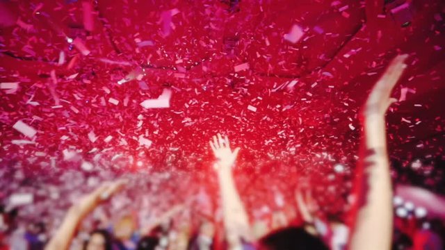 white confetti fall on dancing people against stage with flashing spotlights at wedding party slow motion