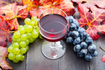 glass of red wine and grapes on black wooden table background