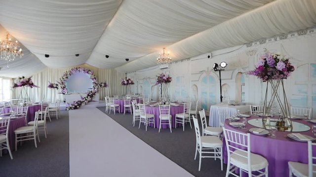 panorama of wonderful empty restaurant hall with purple flowers decoration and white ceiling on wedding day