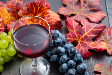 glass of red wine and grapes on black wooden table background