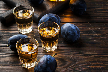 Slivovica - plum brandy or plum vodka, hard liquor, strong drink in glasses on old wooden table, fresh plums, copy space