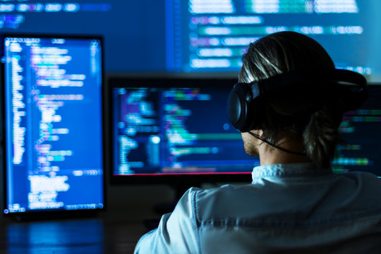 Software developer freelancer man male in headphones work with program code C++ Java Javascript on wide displays at night Develops new web desktop mobile application or framework. Projector background