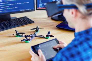 Programmer in virtual reality glasses is controlling FPV drone using tablet. Developer is building...