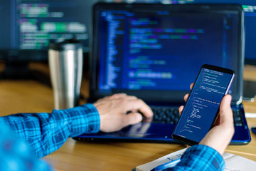 Closeup freelancer hand is holding smartphone with program code. Programmer developer is writing...